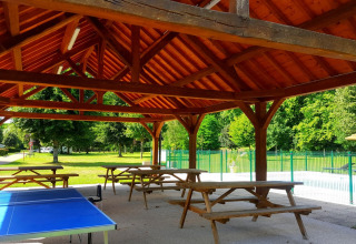 Træpavillon med picnicborde og bordtennisbord i grønt ferieanlæg på Camping Seasonova Le Martinet, Frankrig.