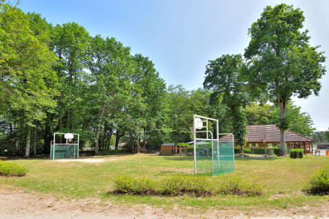 Basketbalvelden in de open lucht omgeven door bomen op Camping Seasonova Etang de la Vallée, Frankrijk.