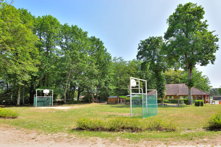 Outdoor basketball courts surrounded by trees at Camping Seasonova Etang de la Vallée holiday park in France.