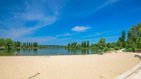 Sunny sandy beach by the lake at Camping Seasonova Vesoul, Bourgogne-Franche-Comté, France, with visitors.