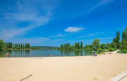 Solrig strand ved søen på Camping Seasonova Vesoul, Bourgogne-Franche-Comté, Frankrig, med få besøgende.
