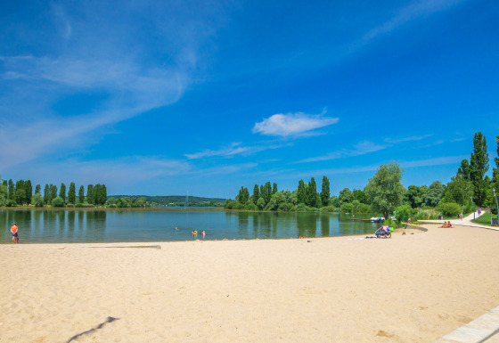 Playa soleada junto al lago en Camping Seasonova Vesoul, Bourgogne-Franche-Comté, Francia, con visitantes.
