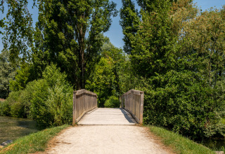 Houten brug over een riviertje omgeven door bomen bij Camping Seasonova Vesoul in Bourgogne-Franche-Comté.
