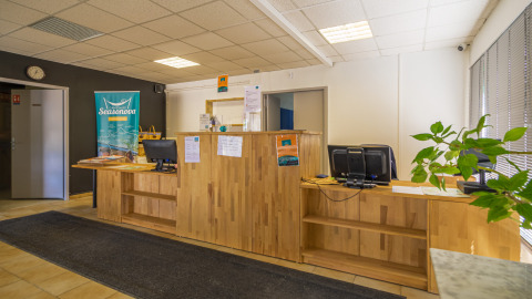 Onthaalruimte van Camping Seasonova Vesoul met houten balie, computers en brochures in Bourgogne, Frankrijk.