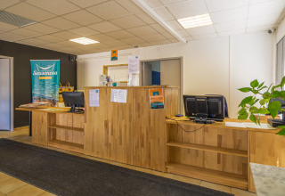 Onthaalruimte van Camping Seasonova Vesoul met houten balie, computers en brochures in Bourgogne, Frankrijk.