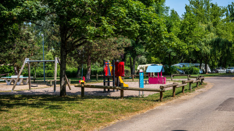 Parque infantil con columpios y juegos coloridos en un camping rodeado de árboles en Bourgogne-Franche-Comté, Francia.