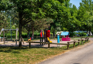 Parco giochi con altalene e attrezzature colorate in un campeggio circondato da alberi in Borgogna-Franca Contea, Francia.