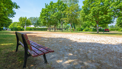Parkbank naast een zandvolleybalveld en weelderige bomen bij Camping Seasonova Vesoul, Bourgogne-Franche-Comté.