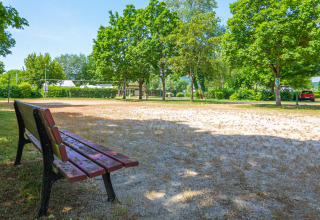 Park bench overlooking a sandy volleyball court and lush trees at Camping Seasonova Vesoul, France.