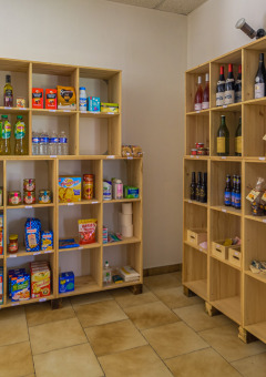 Tienda interior con estantes de madera llenos de comestibles, botellas de vino y una silla azul Seasonova.