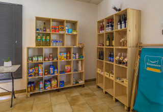 Indoor shop area with wooden shelves filled with groceries, wine bottles, snacks, and a blue Seasonova chair.