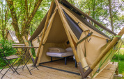 Comfortabele glampingtent met bed en stoelen op houten platform, omgeven door bomen en groen.