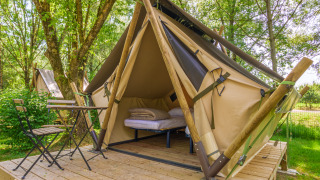 Comfortabele glampingtent met bed en stoelen op houten platform, omgeven door bomen en groen.