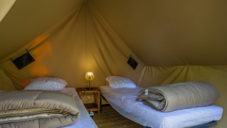 Interior de tienda safari con dos camas individuales, ropa de cama, mesita de noche y lámpara central.