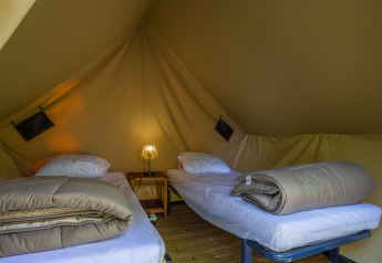 Interieur van een safaritent met twee eenpersoonsbedden, beddengoed, nachtkastje en een lamp tussenin.