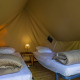 Interior de tienda safari con dos camas individuales, ropa de cama, mesita de noche y lámpara central.
