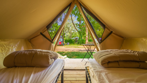 Vista interior de una tienda glamping con dos camas, edredones y entrada abierta hacia un camping verde.