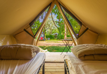 Vista interior de una tienda glamping con dos camas, edredones y entrada abierta hacia un camping verde.