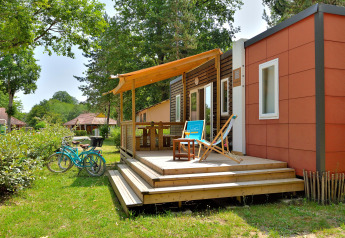 Udendørs scene ved Cottage New Valley, viser en hyggelig terrasse, cykler og grøn beplantning omkring hytten.