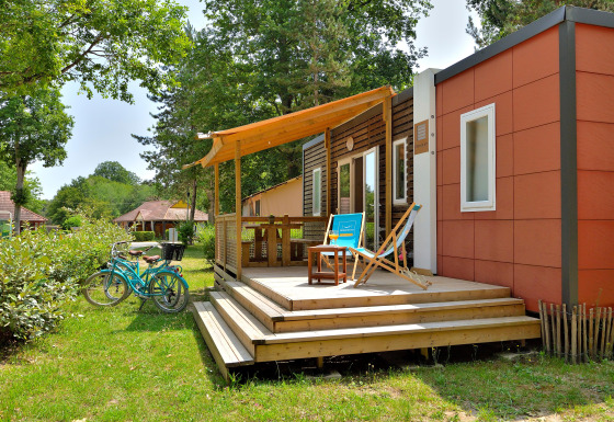 Udendørs scene ved Cottage New Valley, viser en hyggelig terrasse, cykler og grøn beplantning omkring hytten.
