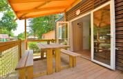 Overdekt houten terras met tafel en banken bij Cottage New Valley, omringd door bomen.