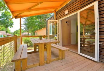 Udendørs terrasse med træbord og bænke ved Cottage New Valley, omgivet af grønne træer.