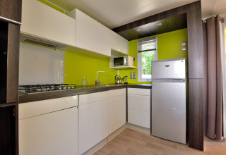 Cocina moderna en esquina en Cottage New Valley, con pared verde lima, muebles blancos y nevera.