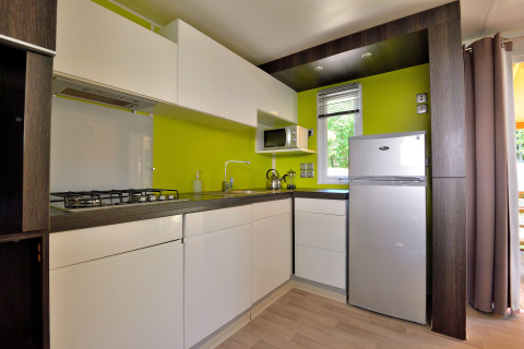 Cocina moderna en esquina en Cottage New Valley, con pared verde lima, muebles blancos y nevera.