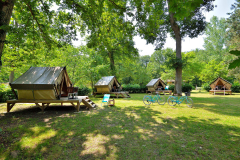 Foto de varias tiendas tipi en un camping verde con dos bicicletas azules y muebles de exterior.