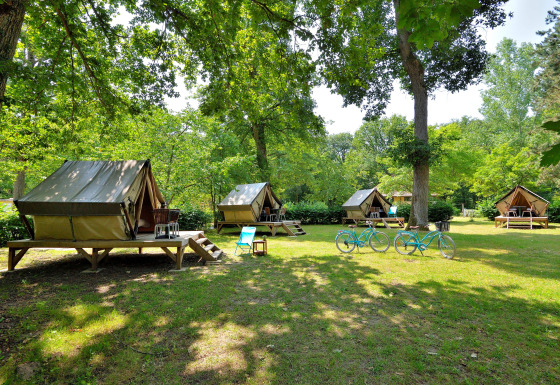 Foto de varias tiendas tipi en un camping verde con dos bicicletas azules y muebles de exterior.