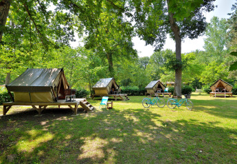 Photo de plusieurs tentes tipi sur un terrain de camping verdoyant, deux vélos bleus et des chaises de jardin.