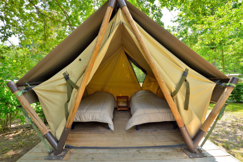 Foto de un tipi con dos camas individuales y suelo de madera, ubicado en un entorno verde ideal para acampar.