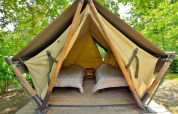 Foto de un tipi con dos camas individuales y suelo de madera, ubicado en un entorno verde ideal para acampar.