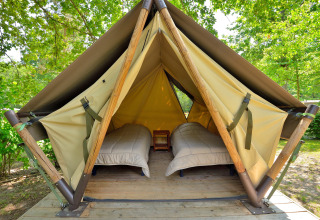 Photo of a teepee tent with two single beds and a wooden floor, set in a peaceful green forest camping area.
