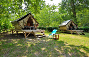 Twee verhoogde tipi-tenten in een groene, bosrijke omgeving met terrassen en relaxstoelen buiten.
