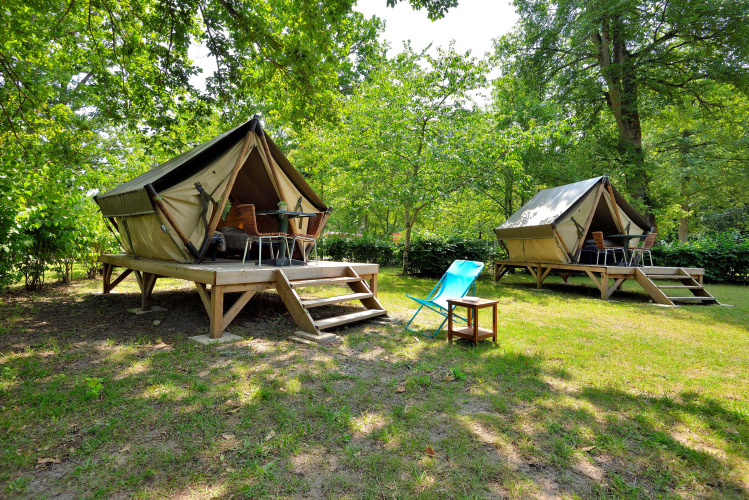 Dos tiendas tipo tipi elevadas en un bosque verde, con terrazas y sillas exteriores para descansar.