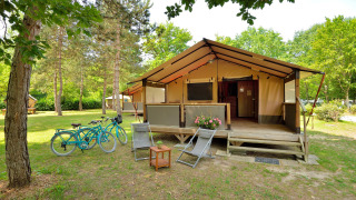 Tienda safari Lodge Victoria con terraza de madera, dos bicicletas y sillas en un entorno natural verde.