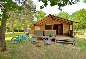 Safari tent Lodge Victoria met houten veranda, twee fietsen en ligstoelen in een groene natuuromgeving.