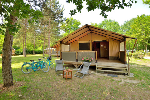 Safari tent Lodge Victoria with wooden veranda, two bikes, and chairs set in a lush, green natural area.