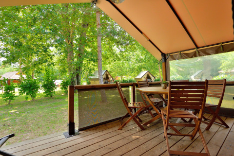 Terraza de madera con muebles de jardín bajo carpa tipo safari en Lodge Victoria, Camping Seasonova Etang de la Vallée.