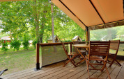 Terraza de madera con muebles de jardín bajo carpa tipo safari en Lodge Victoria, Camping Seasonova Etang de la Vallée.