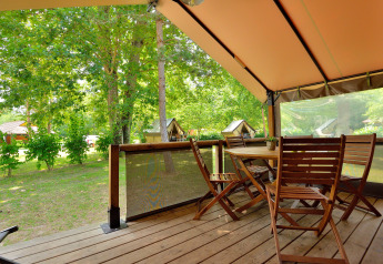 Terraza de madera con muebles de jardín bajo carpa tipo safari en Lodge Victoria, Camping Seasonova Etang de la Vallée.
