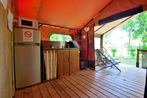Zona de cocina dentro de una tienda safari en Camping Seasonova Etang de la Vallée, con frigorífico y sillas de jardín.
