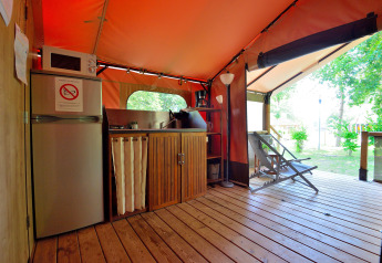 Zona de cocina dentro de una tienda safari en Camping Seasonova Etang de la Vallée, con frigorífico y sillas de jardín.