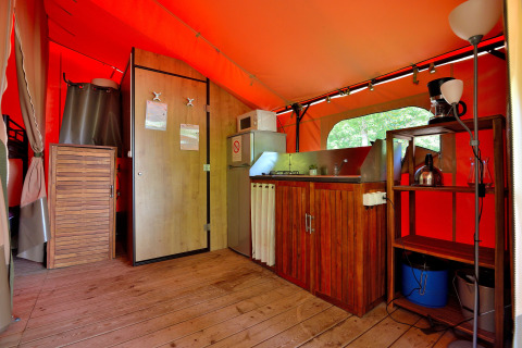 Interno della tenda safari Lodge Victoria con pavimento in legno, cucina e scaffali al Camping Seasonova Etang de la Vallée.