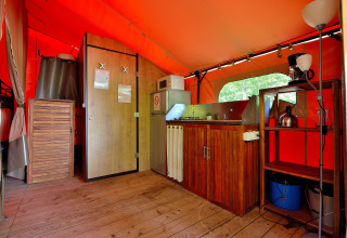 Interior de la tienda safari Lodge Victoria con suelo de madera, cocina y estanterías en Camping Seasonova Etang de la Vallée.