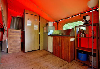 Interior de la tienda safari Lodge Victoria con suelo de madera, cocina y estanterías en Camping Seasonova Etang de la Vallée.