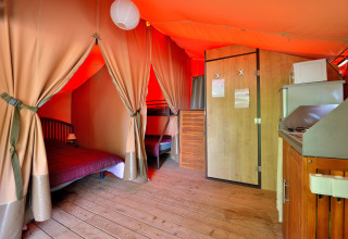 Vista interior de la tienda safari Lodge Victoria con suelo de madera, cama, literas y cocina en camping en Francia.