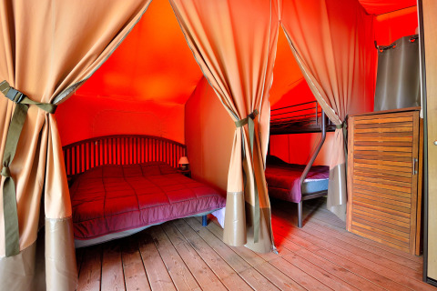 Interior of a safari tent with a double bed and bunk bed at Lodge Victoria, Camping Seasonova Etang de la Vallée, France.