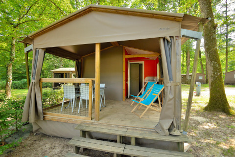 Afbeelding van een Mobilodge-hut met overdekt terras, stoelen, tafel en omgeven door bomen in het bos.